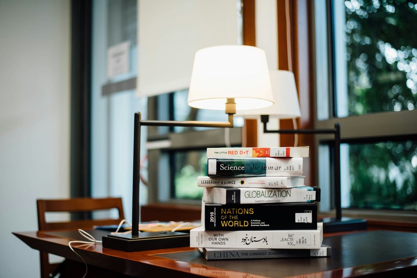 Gestapelte Lehrbücher auf einem polierten Schreibtisch aus Holz.